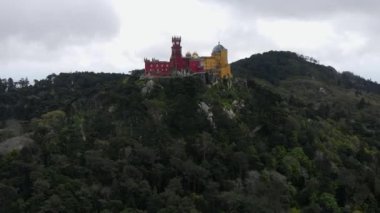 Pena Sarayı 'nın kırmızı ve sarı kuleleri Portekiz' in Sintra kentindeki ormanlık bir tepenin üzerinde yükseliyor. Bulutlu gökyüzü canlı romantik mimariyi geliştirir..