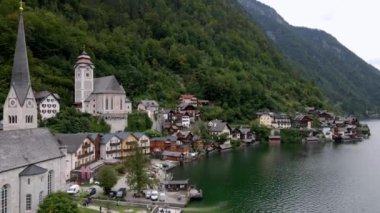 Avusturya 'nın Hallstatt köyünde uzun bir çan kulesi, geleneksel evleri ve orman dağları manzarasını yansıtan bir gölü olan tarihi bir kilise yer almaktadır..