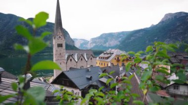 Avusturya 'daki Hallstatt köyü manzarası, Lutheran kilisesinin çan kulesi, geleneksel mimarisi, canlı sarı bir bina ve yemyeşil dağlar..