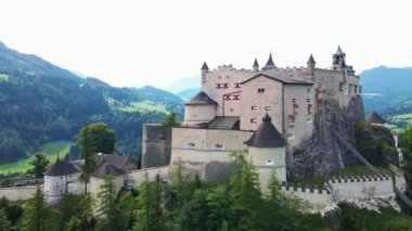 Hohenwerfen Şatosu 'nun ortaçağ mimarisi, taş duvarlar ve taretlerle, Avusturya' nın Salzach Vadisi 'ndeki kayan tepeler ve orman dağlarıyla tezat oluşturuyor..