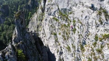 İki dağcı, Avusturya 'da sık ormanlarla çevrili engebeli bir uçuruma tırmandı. Kayalık arazi, ormanın alçak yamaçlarıyla çelişiyor ve yükselişi vurguluyor..