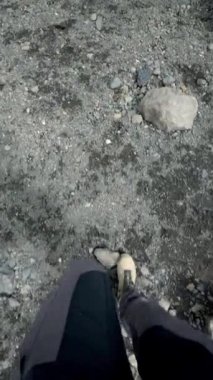 İzlanda 'da kayalık arazide yürüyüş botları ve pantolonları ile yürüyen bir adam. Zemin küçük kayalarla kaplı ve büyük bir kaya görülebilir..