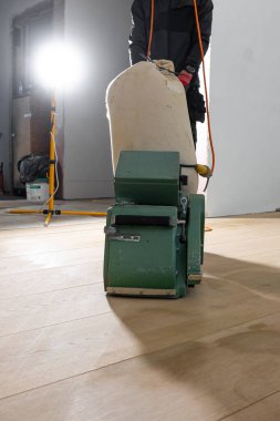 Yeşil zemin cilalama makinesi, yenilenmiş bir odada, aydınlık ahşap bir zeminde, aletler, malzemeler ve parlak bir iş ışığı ile görünür bir şekilde kullanılır..