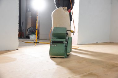 Bir işçi yeşil zemin cilalama makinesi kullanır açık ahşap döşeme üzerinde az döşenmiş kapalı alanda görünür inşaat araçları ile.