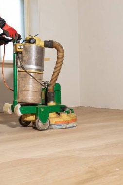 Temiz bir ahşap zeminde eldivenli biri tarafından işletilen yeşil ve sarı yer cilası. Işık, düz odadaki bir pencereden girer..