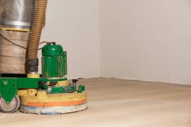 Kısmen kumlu ahşap zeminde beyaz duvarlara karşı toz toplama sistemi olan yeşil ve sarı bir yer cilası..