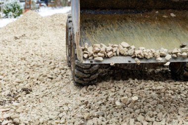 Yere çakıl döken bir damperli kamyonu kapat. Sert lastikleri, yıpranmış metal bir yatağı ve arka planda hafif kar izleri var..