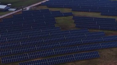 Güneş panellerinin sıraları bir ızgarada dizilmiş küçük kamu binaları ve yenilenebilir enerji alanının sınırlarını işaretleyen bir çitle çimenli bir alanı kaplıyor..