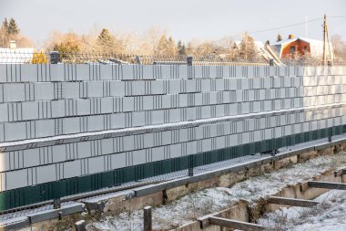Metal bir çitin arkasına yığılmış beton bloklar, yerde kar, korunmasız siperler, ahşap destekler ve arka planda eğimli çatıları olan evler..