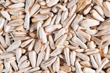 Uzun bej kabuklu ve koyu çizgili ayçiçeği tohumlarının detaylı bir görüntüsü, yoğun bir şekilde düzenlenmiş ve desenli bir desen oluşturur..