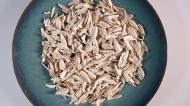 Mavi seramik bir tabağın detaylı bir görüntüsü. İçinde kurumuş ayçiçeği tohumu kabukları var. Kalıplı plaka beyaz arka plandaki açık bej kabuklarla çelişiyor..