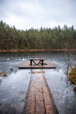 Ahşap bir iskele, sık ve yeşil bir ormanla çevrili kırmızı tırabzanlar ve bir bankın olduğu bir platforma götürür. Gölün buzlu yüzeyi dağınık buz kütlelerine sahiptir..