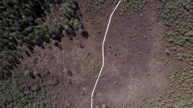 Zigzag ahşap bir kaldırımın havadan görünüşü. Kuru otlakları aşıyor, seyrek bitki örtüsü, küçük ağaçlar ve görülebilir gölgeler araziye derinlik katıyor..