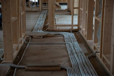 İnşaat halindeki bir evin iç manzarası, ahşap çerçeve, beton zemin ve erken safhalardaki organize havalandırma veya elektrik kanalları.