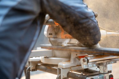 Eldivenli eldiven kılavuz materyali ile kullanılan dairesel testereyi kapat. Toz parçacıkları havada yüzerek aktif inşaat çalışmalarını vurguluyor..