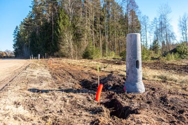 Beton ışık direkleri, siperler ve elektrik işaretiyle toprak yol boyunca inşaat alanı. Uzun ağaçların ormanı kuru çimenler ve toprakla sınırlıdır..