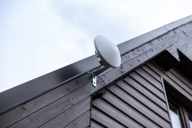 Karanlık ahşap çatılı bir evin çatısına monte edilmiş bir uydu anteni Wi-Fi yönlendirici, bulutlu bir gökyüzüne karşı kurulmuş..
