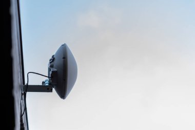 Görünür kablolarla binanın dışında metal bir desteğe monte edilmiş bir WiFi yönlendirici. Arka planda yumuşak bulutlu berrak bir gökyüzü var.