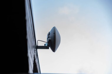 Anthena adında bir Wi-Fi yönlendirici özel bir evin dış duvarına monte edilmiştir. Metal bir desteğe ve görünür kablolara sahiptir. Açık mavi gökyüzüne ayarlıdır..