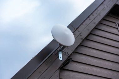 Beyaz dairesel Wi-Fi yönlendirici özel evin çatı kaplamasına eklenmiş koyu kahverengi çatı panelleri kapalı gökyüzü altında..