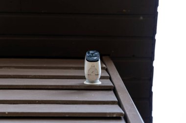 Siyah kapaklı beyaz silindirik bir Wi-Fi yönlendirici yatay ahşap levhaların üzerinde duruyor. Arka planda özel bir evin açık bir alanında koyu ahşap bir duvar var..