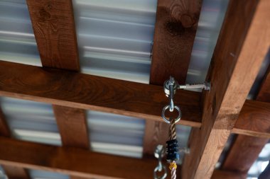 Bükülmüş metal çatıyı destekleyen ahşap kiriş yapısını kapatın. Siyah plastik kabzalı bir ip metal kanca ve göz sürgüsüyle sağlamlaştırılır..