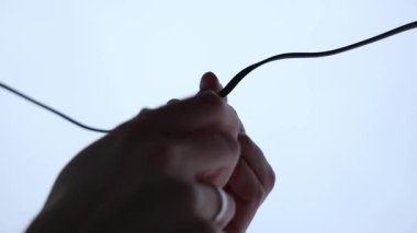 Bir LED ampulü, parlak ve minimal arkaplan üzerine kurulmuş siyah bir sokete vidalayan iki elin yakın plan.