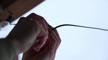 Bir LED ampulü, parlak ve minimal arkaplan üzerine kurulmuş siyah bir sokete vidalayan iki elin yakın plan.