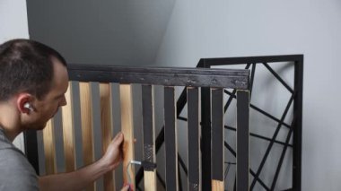 Bireysel olarak, kablosuz kulaklık takarken ahşap ve metal çerçeve yapısını, muhtemelen mobilyayı ayarlıyor. Geometrik metal çerçeve yakınlarda duruyor..