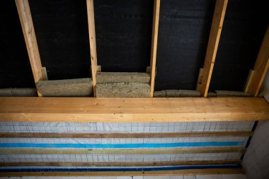 Kısmen inşa edilmiş bir duvar ya da tavanda fibröz yalıtım malzemesi ile korunmasız ahşap kirişler, katmanlı tahtalar ve yapıya benzer bir şebeke içeriyor..