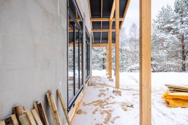 Büyük cam pencereleri ve tahta kirişleri olan, etrafı karla kaplı ve kar tozlu ağaçlarla çevrili modern bir bina..