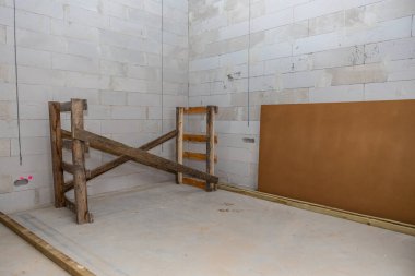 İç mekan beyaz beton blok duvarlar, ahşap geçici bir yapı, eğimli bir tahta ve sol duvarda pembe bir işaret var..