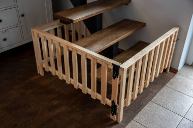 Açık renkli güvenlik kapısı olan ahşap bir merdiven, fayanslı zemin ve modern ev dekorasyonunda siyah düğmeleri olan beyaz dolap..