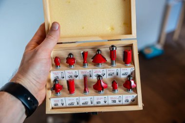 Bir el tarafından tutulan açık ahşap bir kutu etiketli yuvalarda kırmızı yönlendirici parçaları içerir. Köpük dolgusu kapağı çiziyor. Ahşap zeminli bulanık bir iç mekan görülebilir..