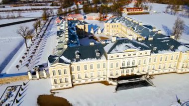 Letonya 'daki Rundale Sarayı karla çevrili, yukarıdan görülüyor. Açık sarı cephe, ağaçların düzgün hizalandığı beyaz manzarayla çelişiyor..