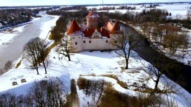 Bauska Kalesi Letonya 'da kırmızı kiremitli çatıları ve ortaçağ mimarisi olan karlı bir manzaranın ortasında duruyor. Çıplak ağaçlar ve açık araziler kış sahnesini tamamlıyor..