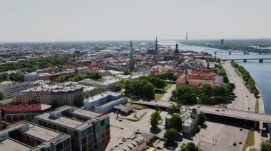 Bu görüntü Riga 'nın şehir manzarasını Aziz Peter Kilisesi kulesi, Daugava Nehri, bir köprü ve Riga TV Kulesi ile birlikte, tarihi ve modern mimariyi harmanlayarak gösteriyor..