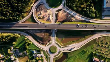 Otoyol üst geçidinin altında bir kavşağın yer aldığı, orman arazileri ve konut binalarıyla çevrili bir kavşağın havadan bakış açısı..