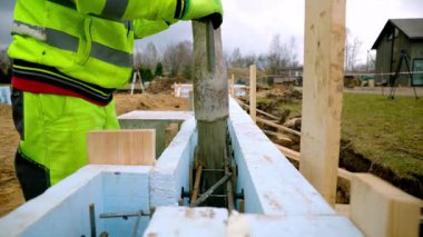 Yüksek görüş mesafesi olan bir inşaat işçisi, mavi yalıtım panelleri ile döşenmiş, kırsal bir ortamda demirle görülebilen biçimsel işlere beton döküyor..