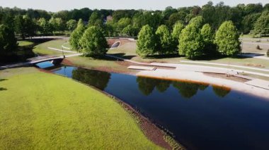 Bir park modern eğimli bir köprüye sahip dolambaçlı bir nehre sahiptir. Ağaçlar çevreyi sarıyor, sakin sulara yansıyor, yürüme yolları var..