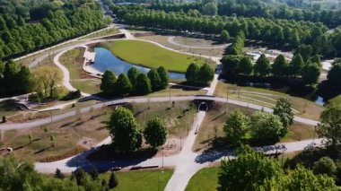 Hava perspektifi, bir parkın dolambaçlı yolları, merkezi bir gölet, köprüler ve çevreleyen ağaçlarla çevrili yerleşim yerlerini yakalar ve simetrisini vurgular..