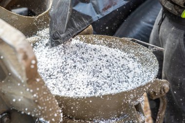 Beyaz granüller siyah bir çantadan dökülür gibi metalik bir kapta yaklaşın, makineler ve yan tarafında kısmen görünür bir işçi.