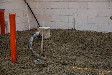 Beton, iki turuncu dikey boru ve kullanımda bir hortumla hazırlanmış bir zemin alanı olan kapalı bir inşaat alanı..