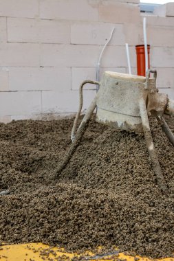 Toplam malzeme, açık renkli beton blok duvarlar, görünür borular ve kırmızı silindirik bir nesnenin yer aldığı bir inşaat alanı..