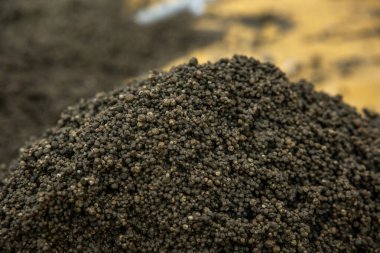 Büyük bir yığın içindeki küçük, koyu taneciklerin detaylı bir görüntüsü, uzaktaki bulanık kahverengi yüzeyle çelişiyor, dokuyu ve tonu vurguluyor..