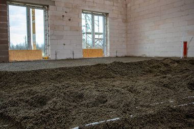 Beyaz tuğlalı duvarlar, beton zemin, geniş pencere aralıkları, iskele ve sağda kırmızı bir boru bulunan inşaat halindeki iç alan..