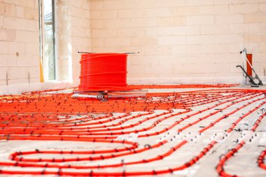 İnşaat alanı içinde kırmızı zemin altı ısıtma boruları desenli, hafif tuğlalı duvarlar, bir pencere ve köşede bir boru tesisatı var..