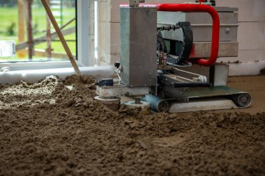 Kırmızı saplı beton seviyelendirme makinesi içerideki ıslak malzemeyi çalıştırır. Doğal ışık geniş bir pencereden girer ve bulanık yeşil çevreyi ortaya çıkarır..