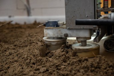 Estrich betonunu zeminin altındaki ısıtma borularının üzerine döşeyen bir makineyi kapatın. Görünür boruları ve beyaz duvarları olan bir inşaat alanında..