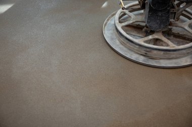 Dairesel metal bıçaklı bir güç malası yeni döşenmiş beton zemini parlatıyor, odaklanmış aydınlatma altında dokuyu ve parıltıyı vurguluyor..